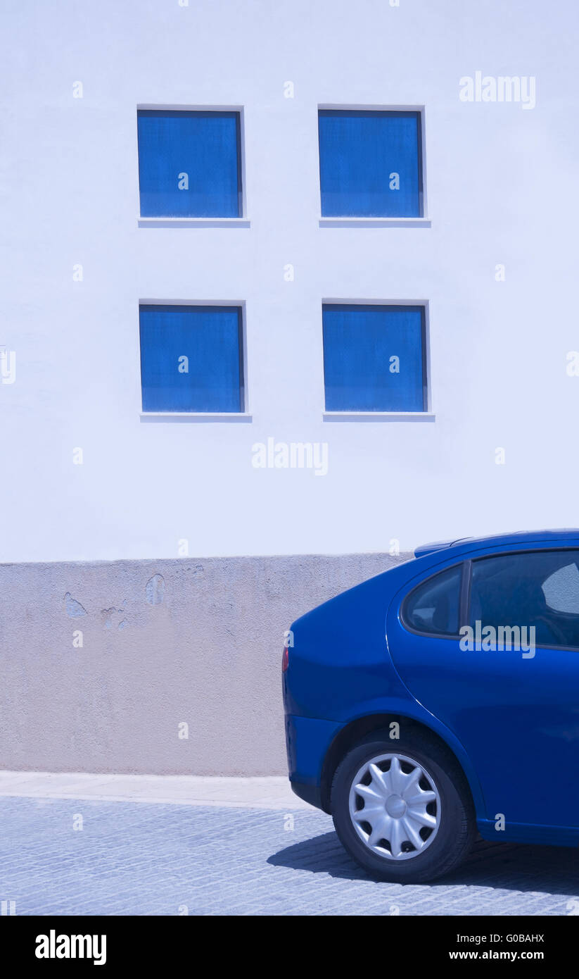 Four blue windows on sunlit white wall and rear of Stock Photo