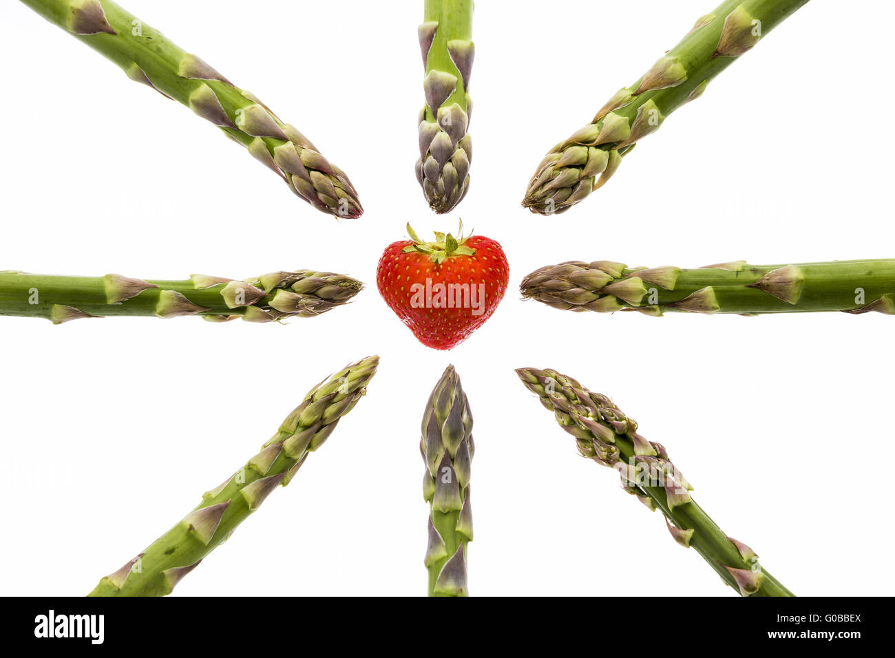 Eight asparagus tips pointing at one strawberry Stock Photo