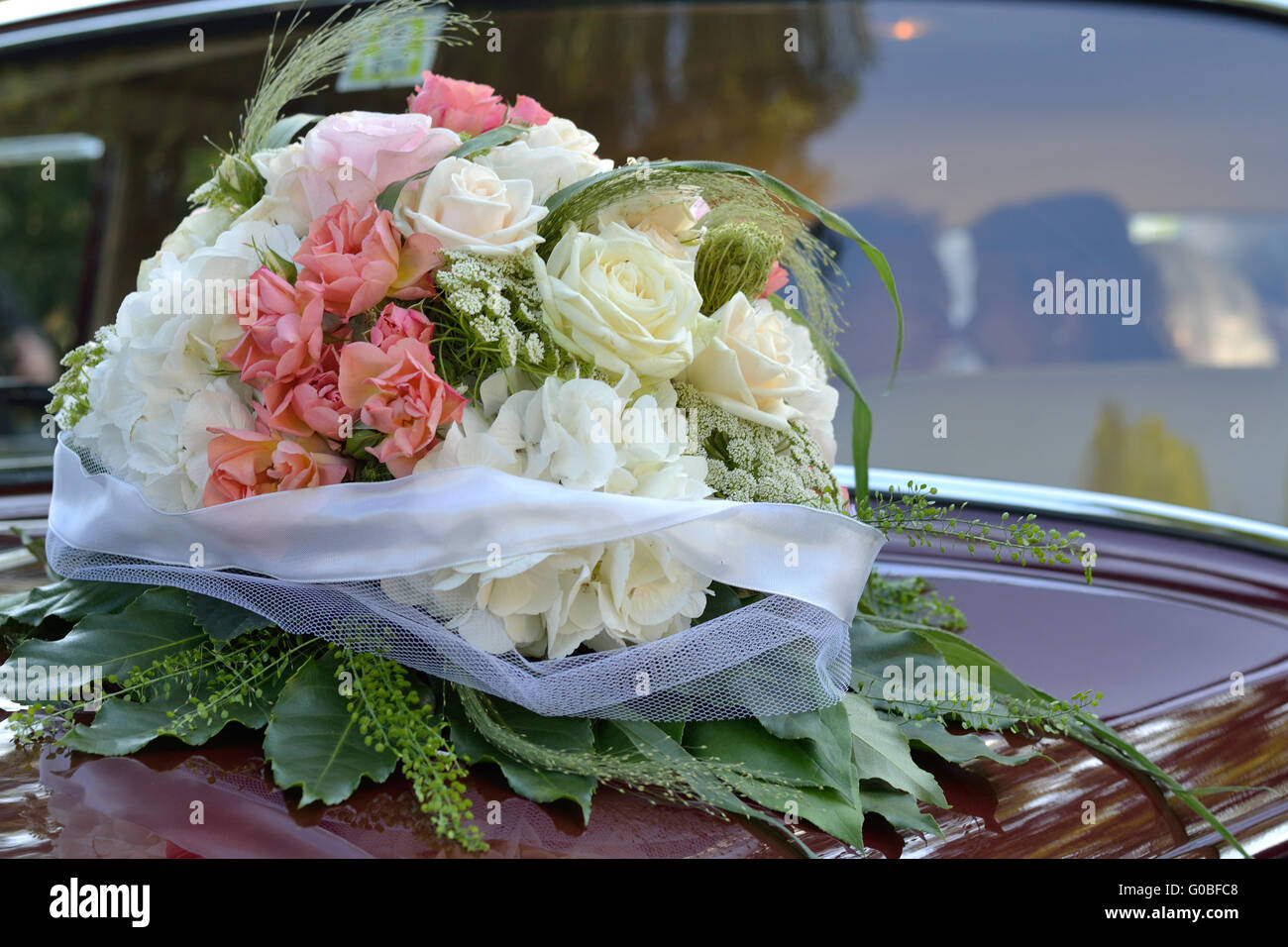 Rose bouquet on wedding car with bride and groom Stock Photo