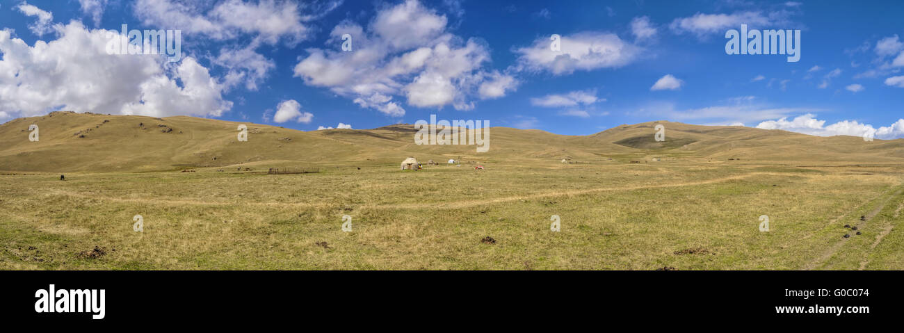 Scenic panorama of green grasslands in Kyrgyzstan with traditional nomadic yurt Stock Photo