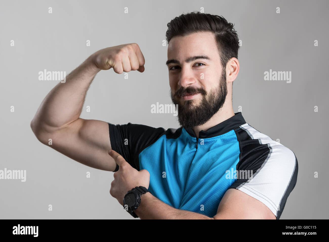 Achievement concept. Portrait of young cyclist flexing his bicep muscle smiling at camera over gray studio background Stock Photo