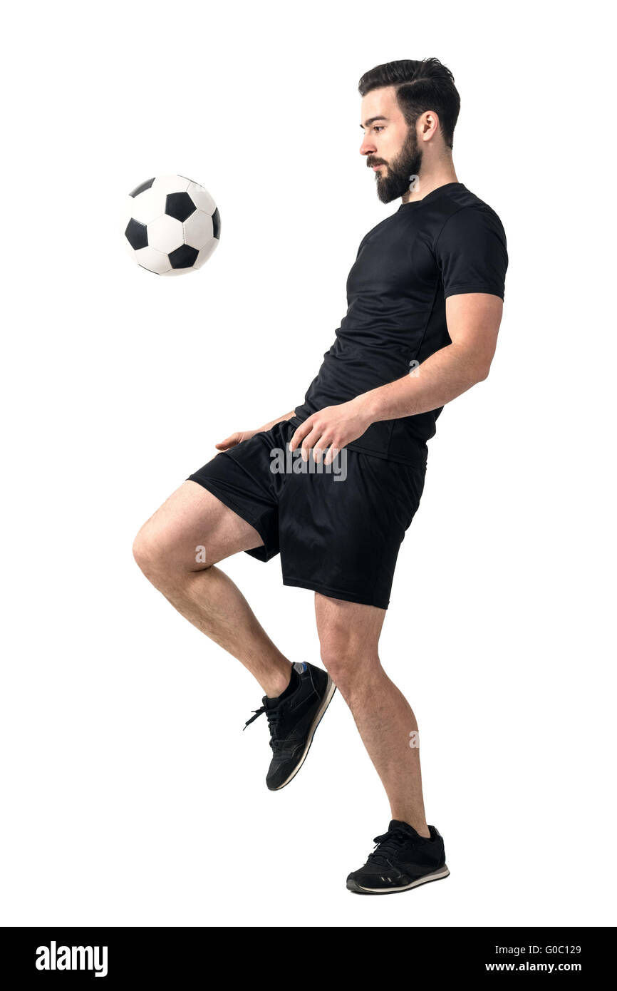 Side view of football or futsal player juggling ball with his knee. Full body length portrait isolated over white background. Stock Photo