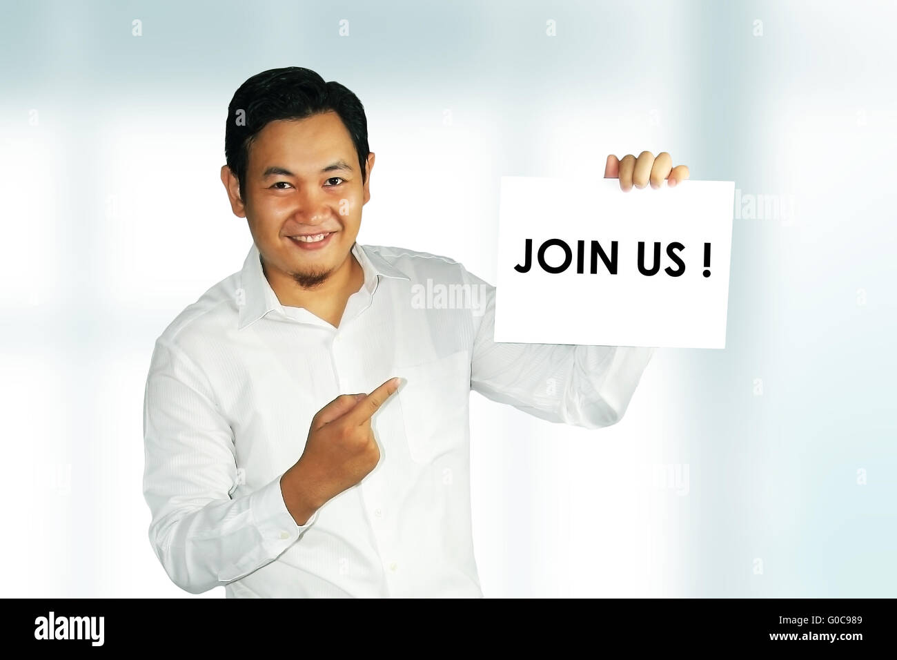 Image of a young Asian male holding white paper with Join Us words written on it over bright background Stock Photo