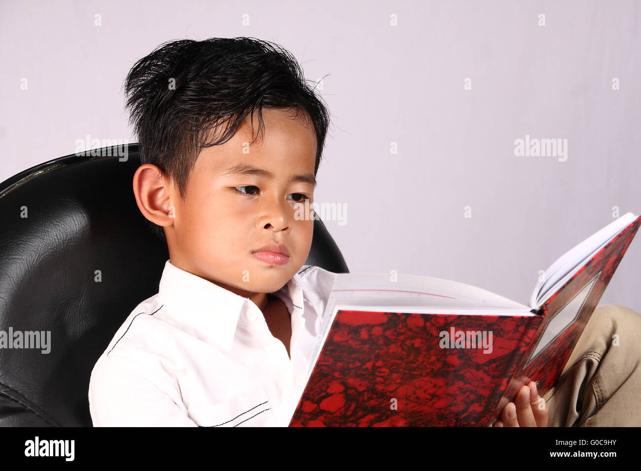 Smart Asian boy reading book while sitting on chair Stock Photo