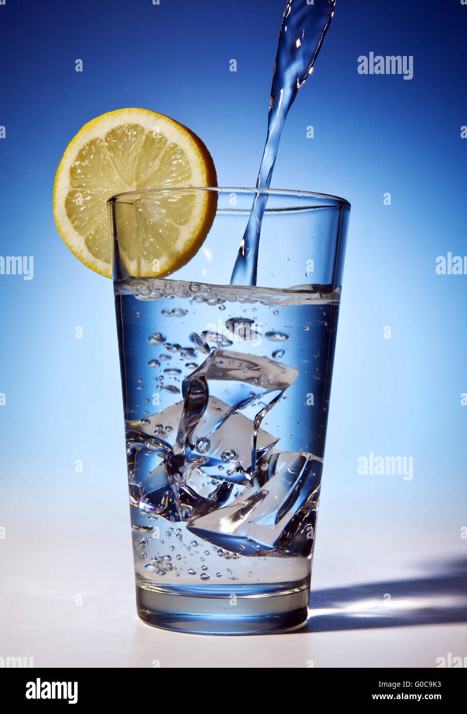 Water is poured into a glass with ice cubes and le Stock Photo