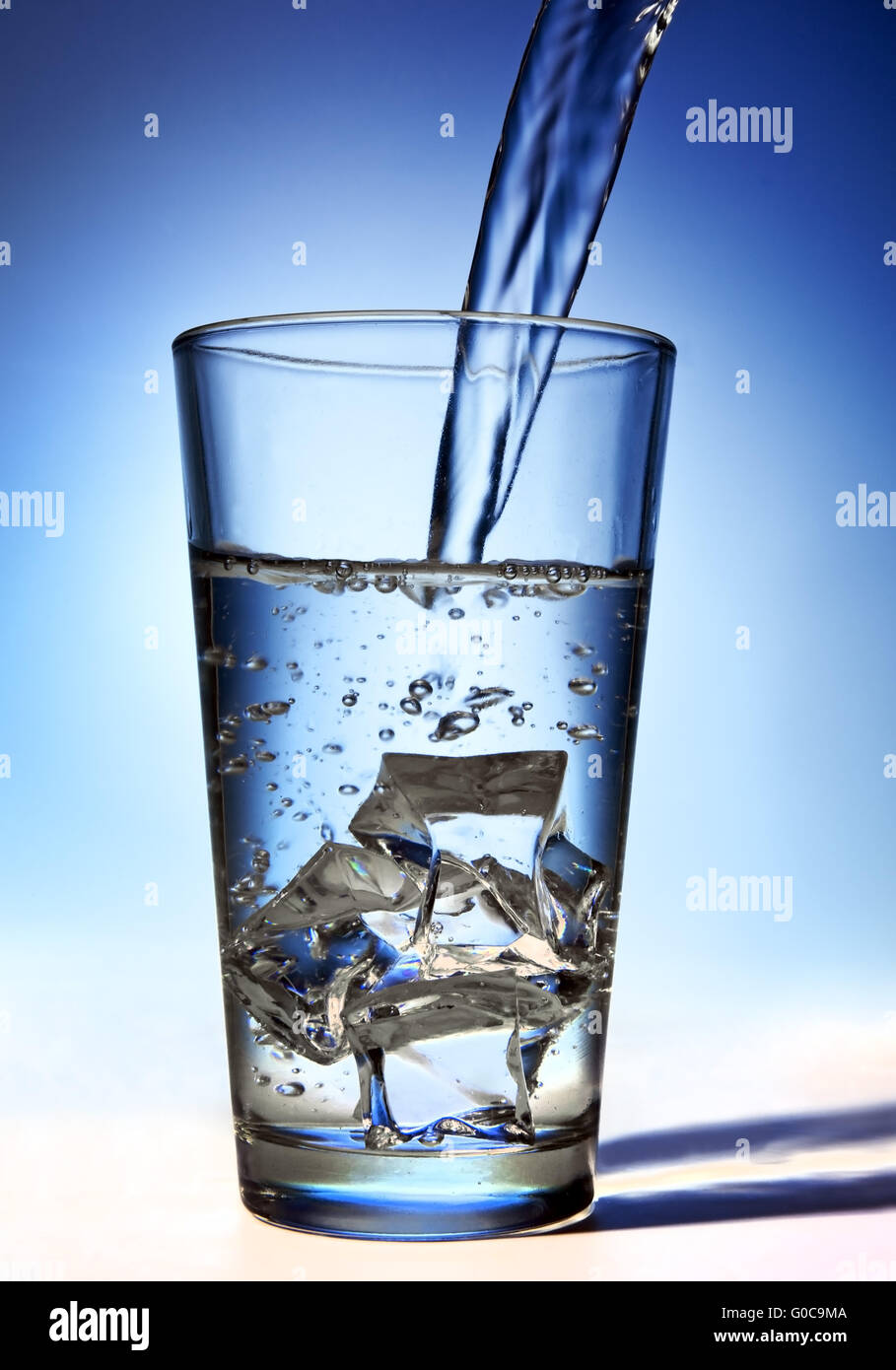 Water is poured into a glass with ice cubes Stock Photo