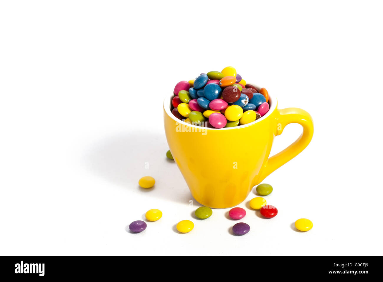 Colorful dragees in small yellow colored cup on white Stock Photo