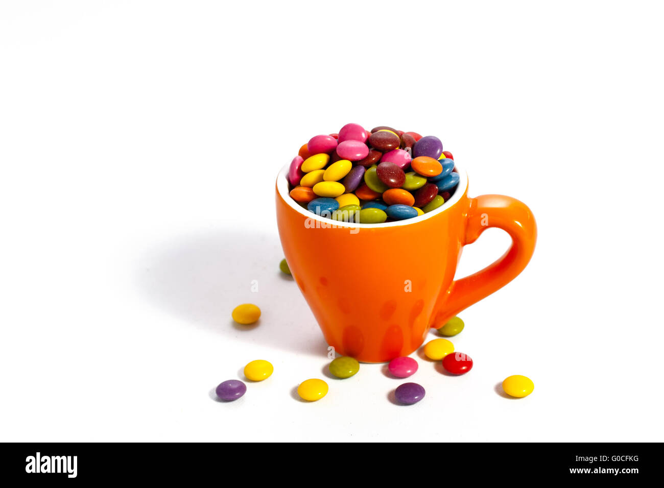 Colorful dragees in small orange colored cup on white Stock Photo