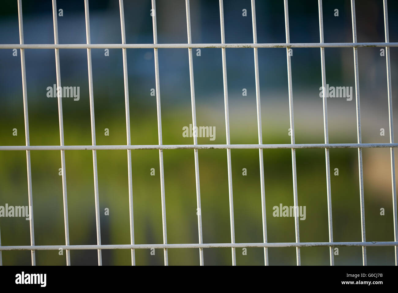 A white wire fence slightly leaning to the left with a very blurred background. Stock Photo