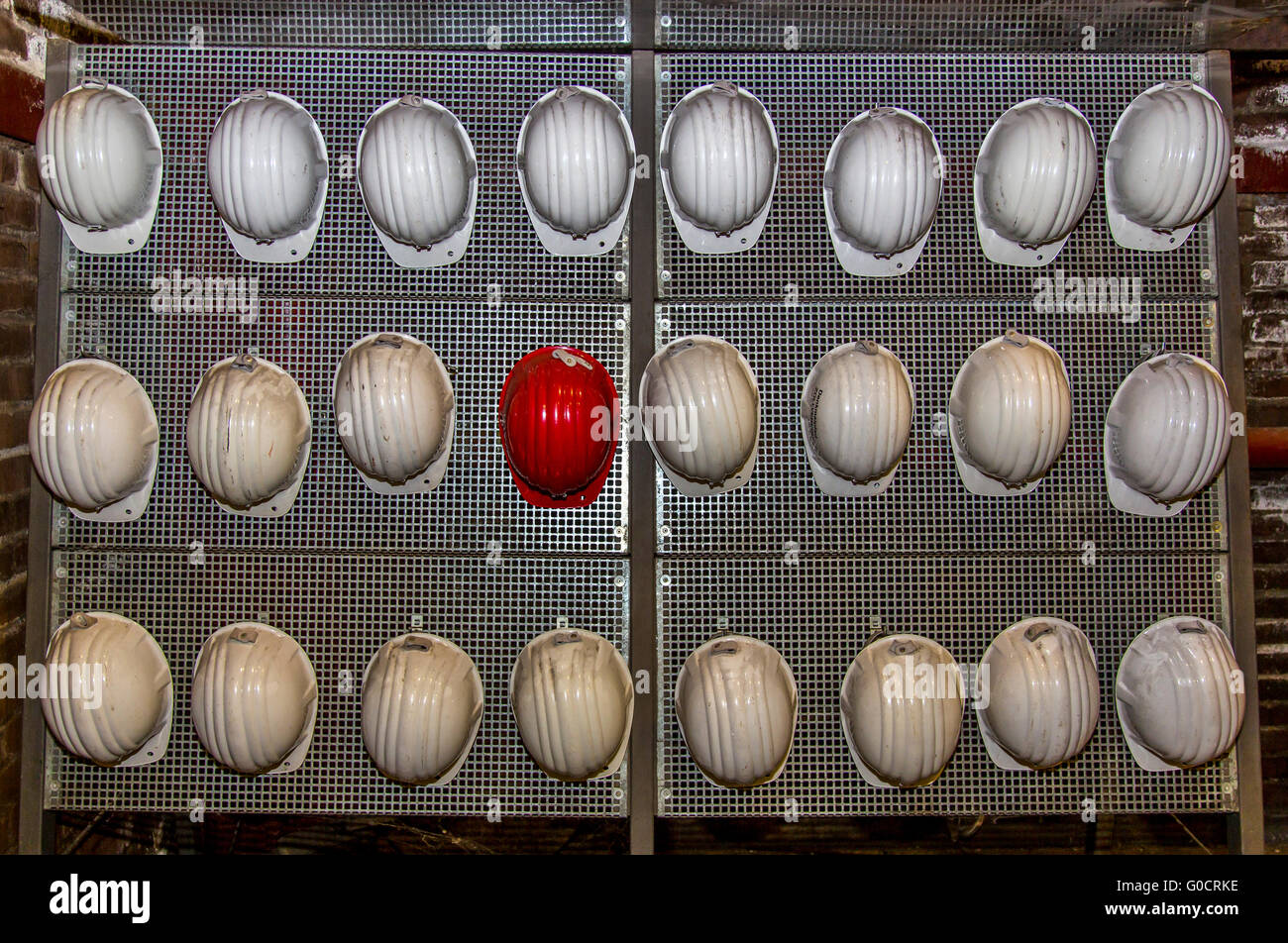 Many white hard hat and a red hard hat hanging on a wall, for visitors
