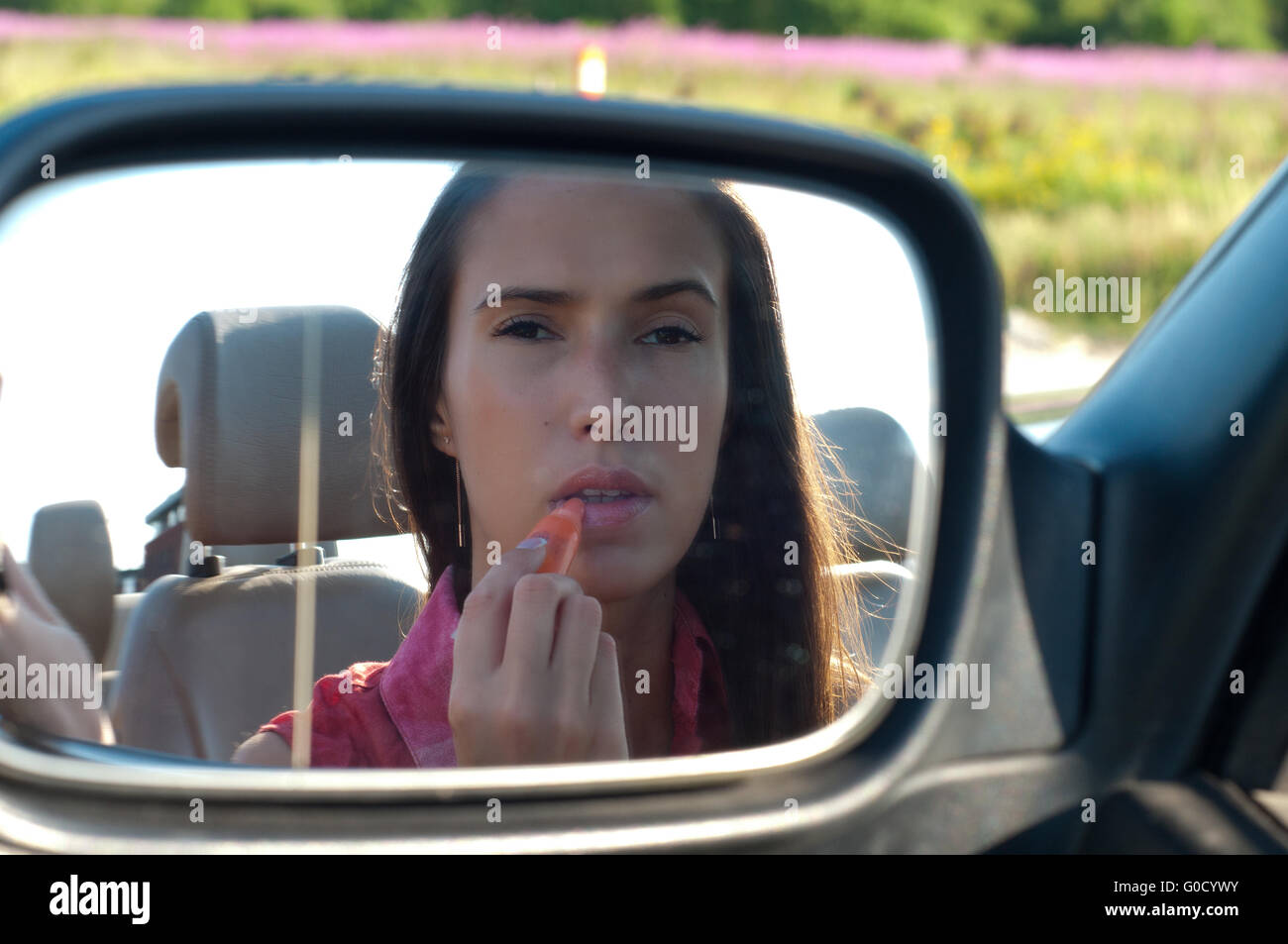 Woman applying lipstick looking at car mirror Stock Photo