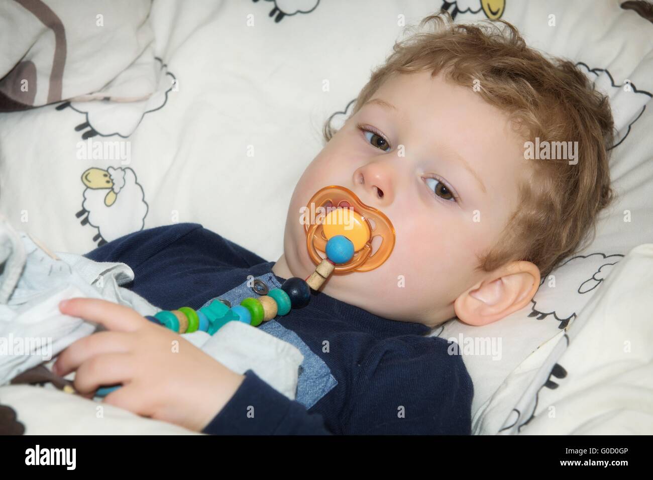 2-year-old boy with pacifier before falling asleep in bed Stock Photo