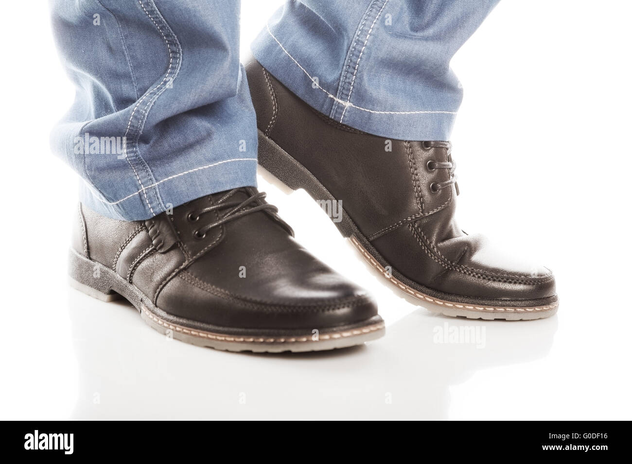 Feet in blue jeans and shoes with laces on a white background Stock