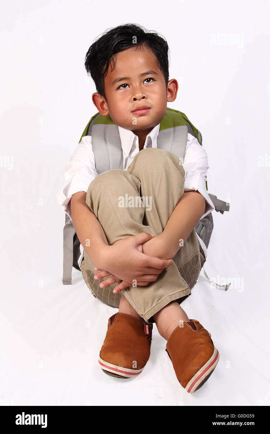 Young Asian student boy dreaming of something while squat sitting and hold his knees in his arms Stock Photo