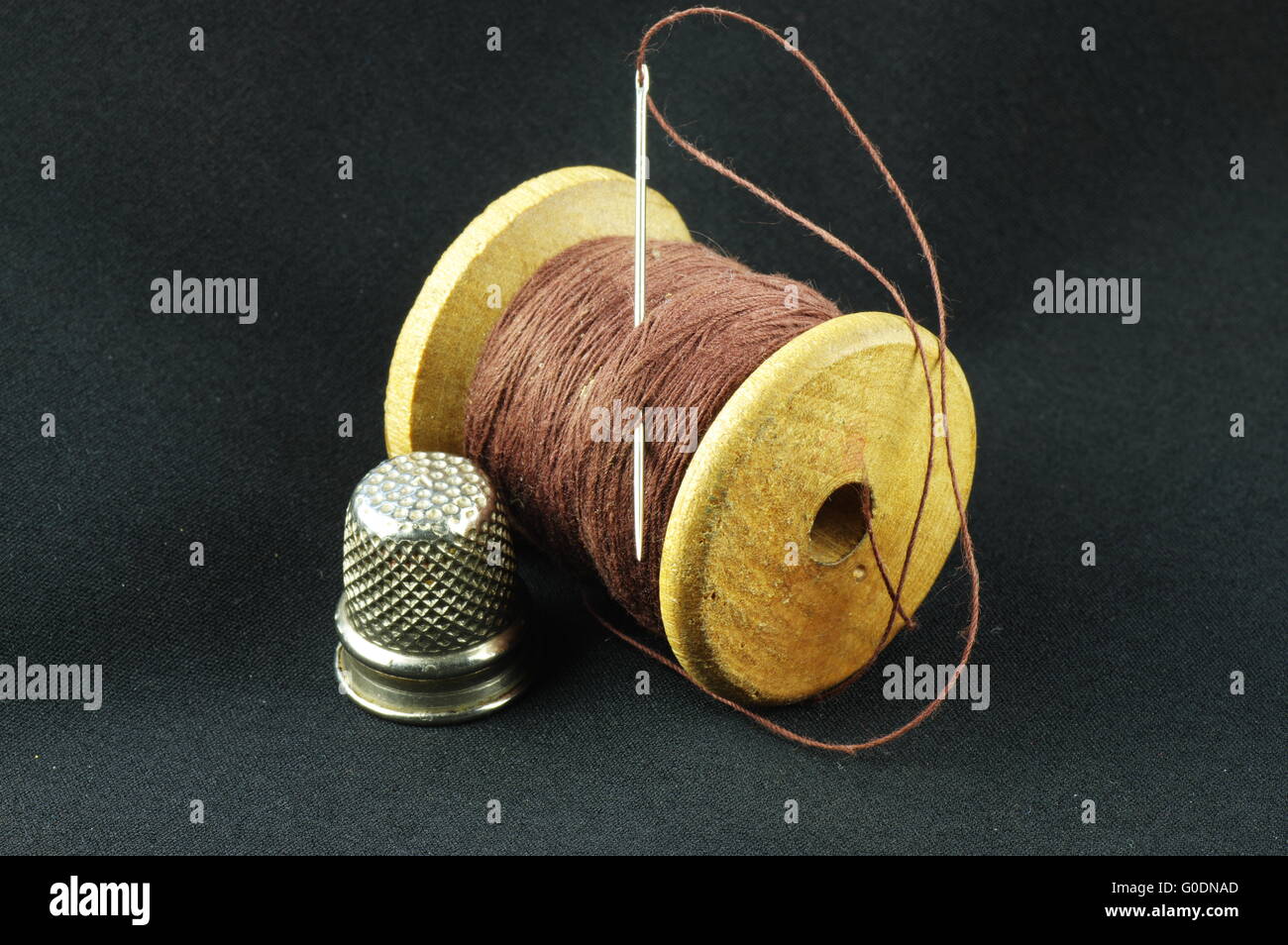 Wooden spool of thread with a needle and a thimble on a dark fabric. Stock Photo