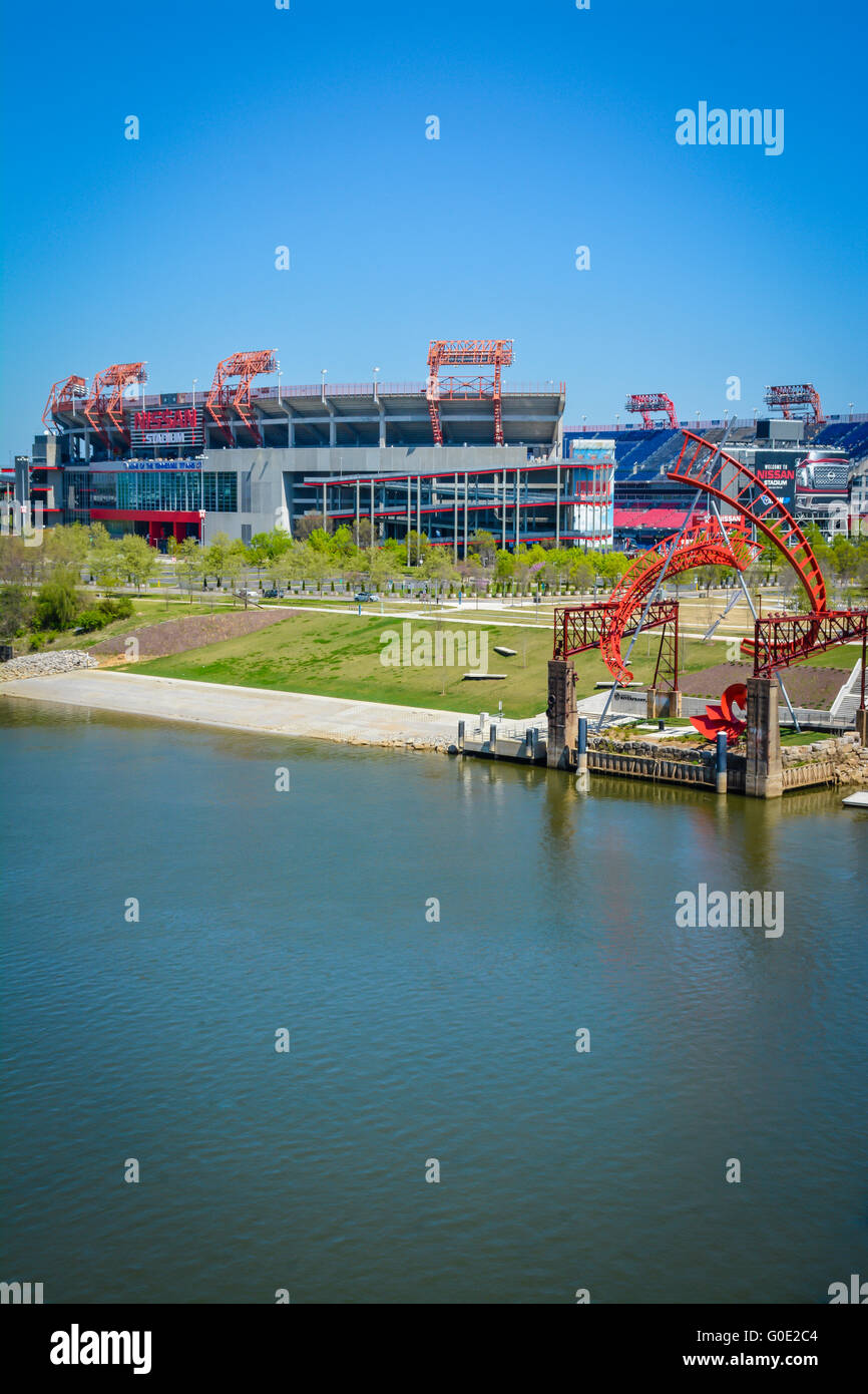 View across the Cumberland River in downtown Nashville TN towards the NFL team Titans' Nissan stadium with 'Ghost Ballet' art displayed on waters edge Stock Photo