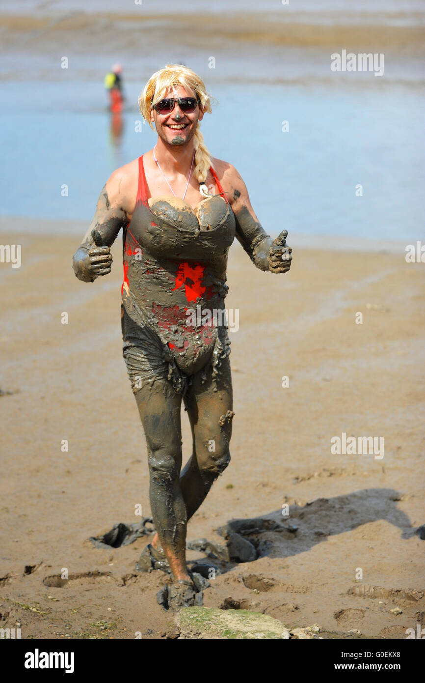 Maldon, Essex, UK. 1st May, 2016. A competitor, wearing a blond wig and falsies, looking happy and giving a thumbs up as he approaches the finish line of the annual Maldon Mud Race in Maldon, east England. Originated in 1973, the race involves competitors racing around a course through the River Blackwater in Essex at low tide. Credit:  Michael Preston/Alamy Live News Stock Photo