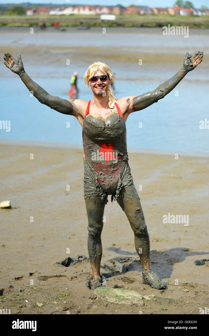 Maldon, Essex, UK. 1st May, 2016. A competitor, wearing a blond wig and falsies, looking happy as he approaches the finish line of the annual Maldon Mud Race in Maldon, east England. Originated in 1973, the race involves competitors racing around a course through the River Blackwater in Essex at low tide. Credit:  Michael Preston/Alamy Live News Stock Photo