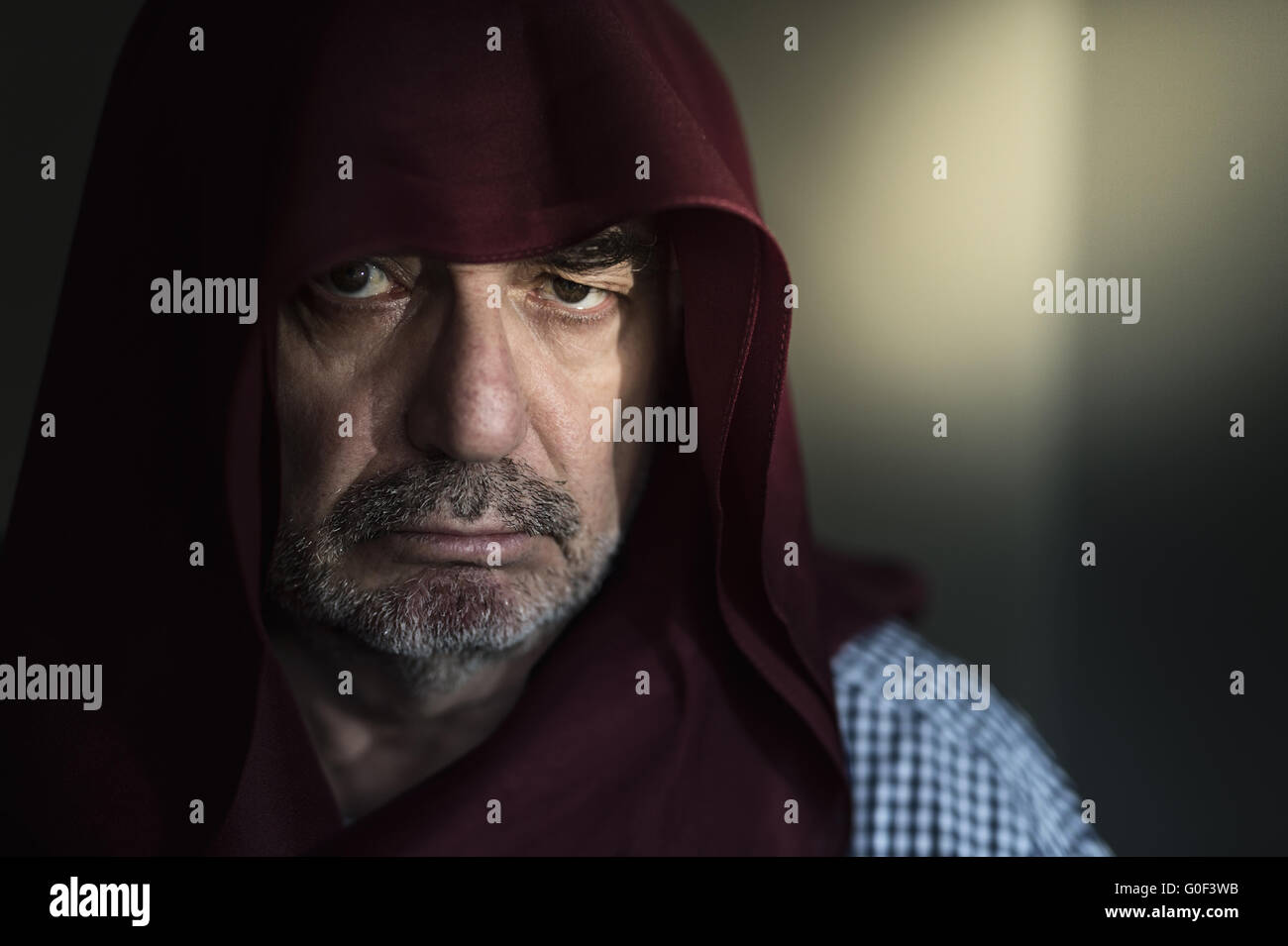 An old man with hood in the side light of a window. Stock Photo