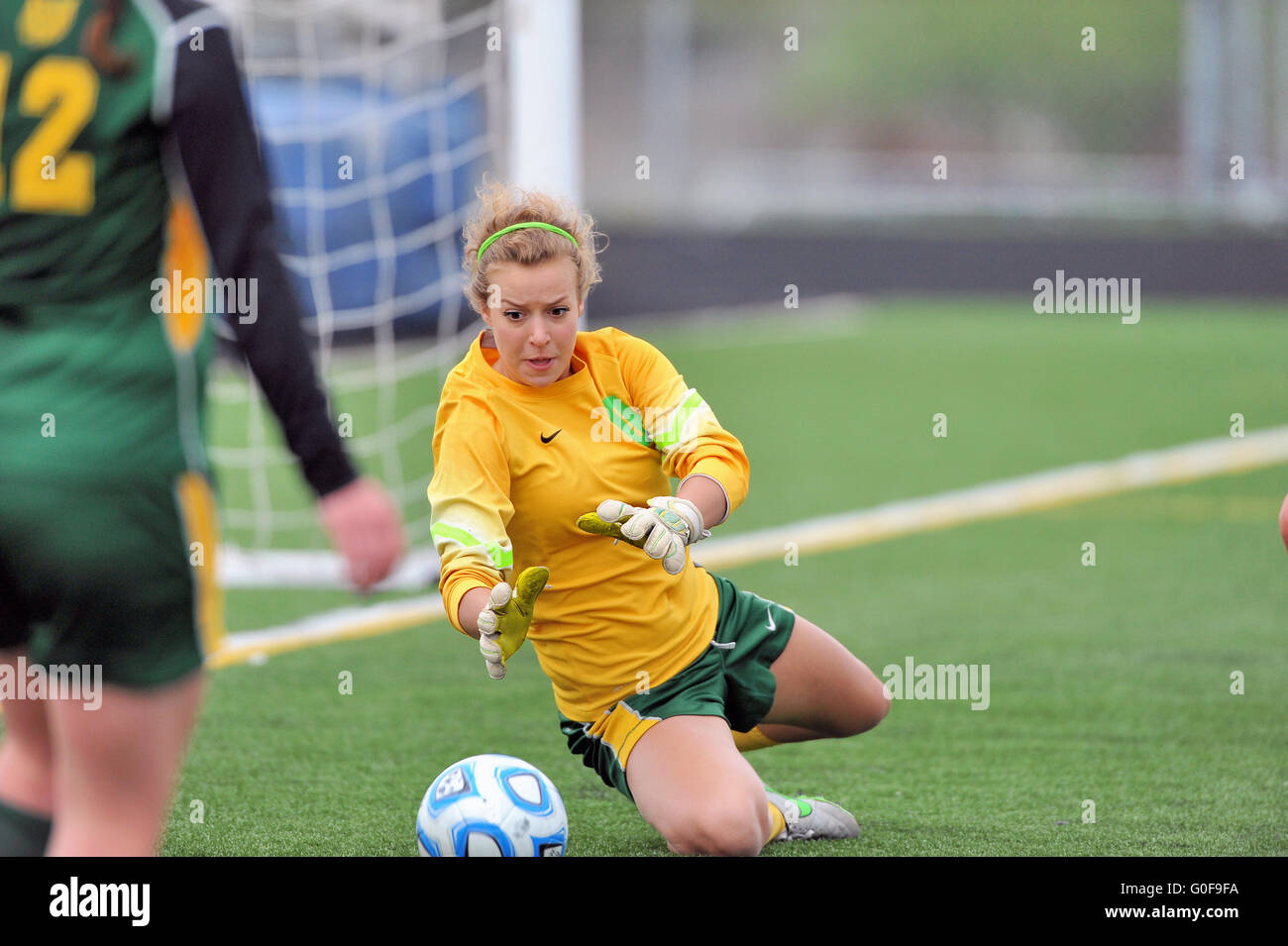 Keeper ranging out from her goal to make a sliding save during a high school soccer match. USA. Stock Photo