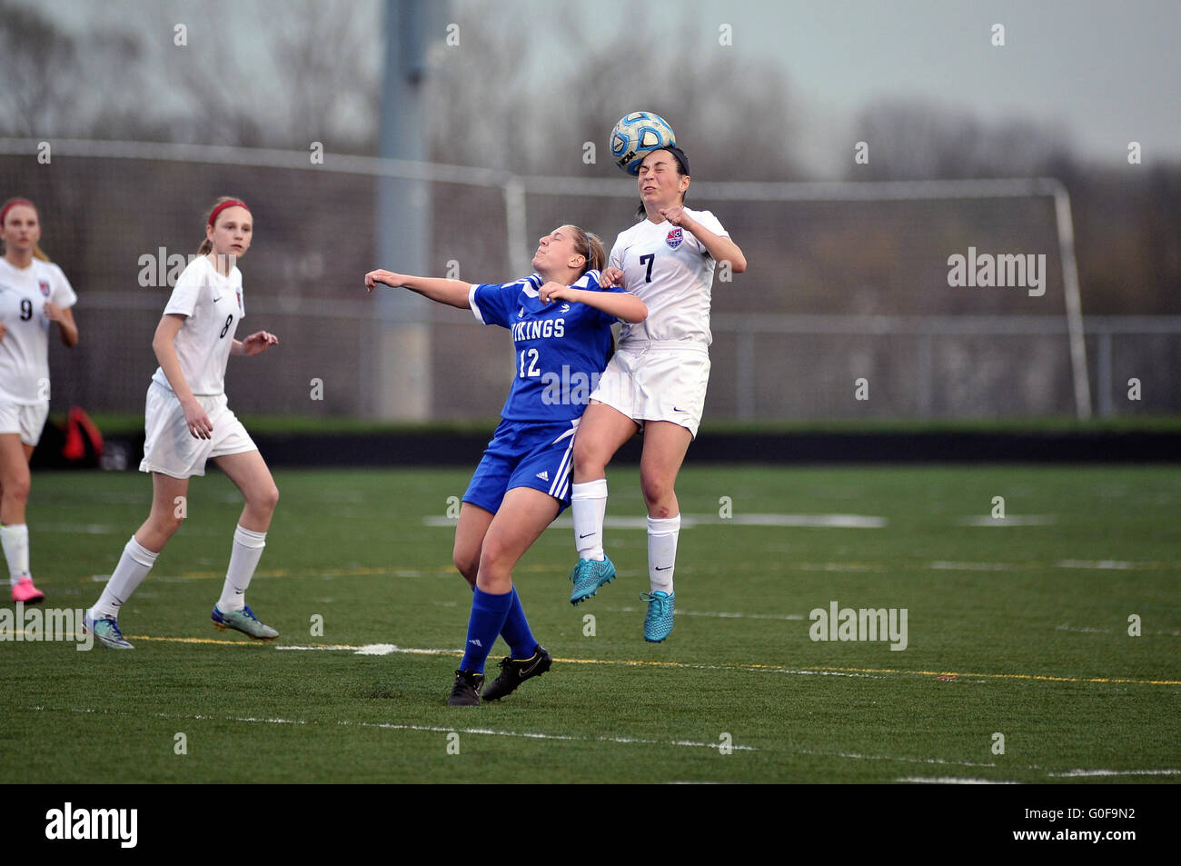 A player rising above the turf and an opponent to execute a header during a high school soccer match. USA. Stock Photo