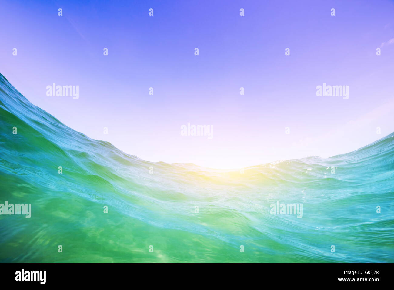 Dynamic water wave in the ocean. View from the waterline. Underwater and blue sunny sky. Stock Photo