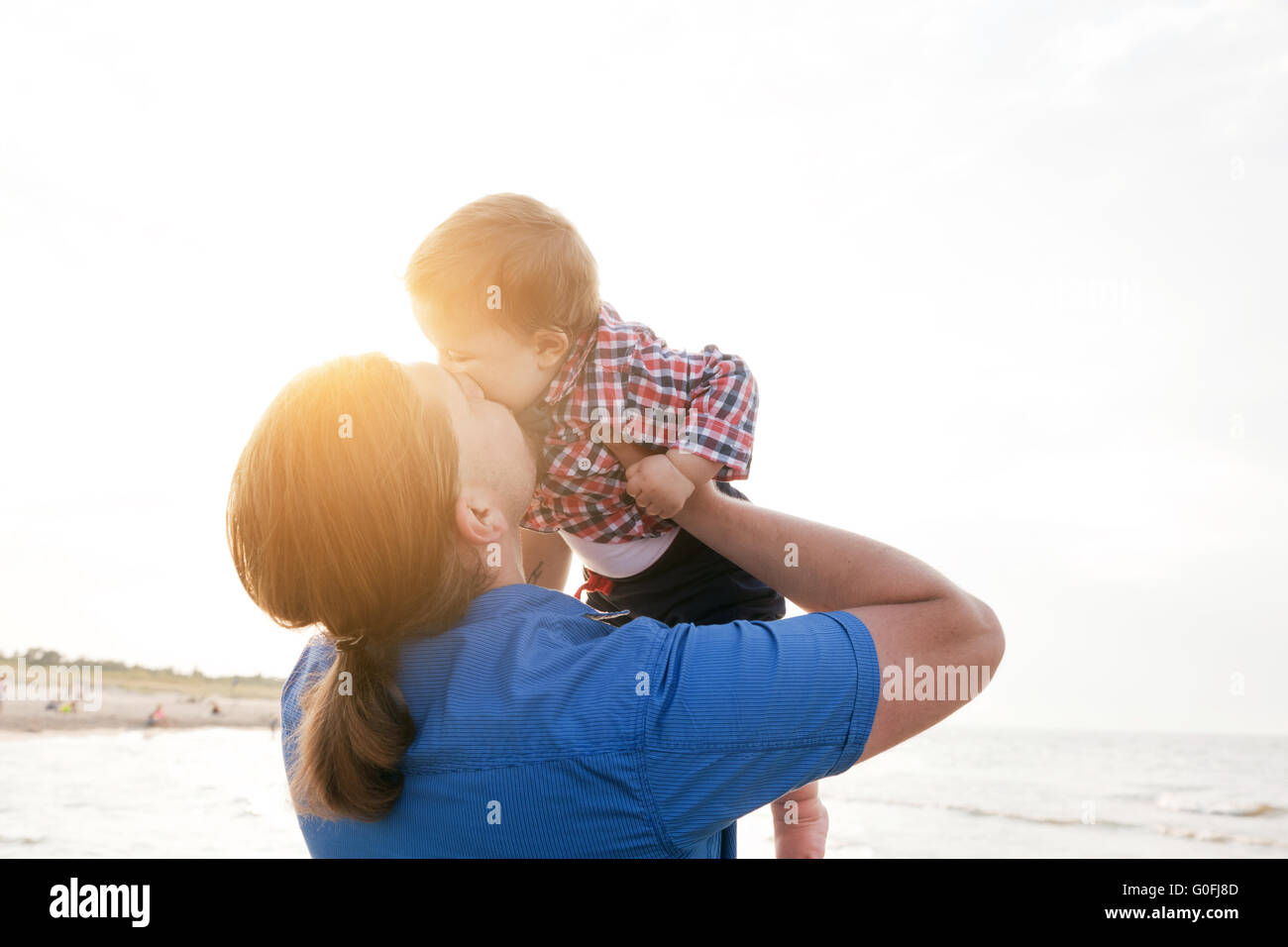 Young father holding his child up in the air on the beach and kissing with love. Son and parent bond Stock Photo