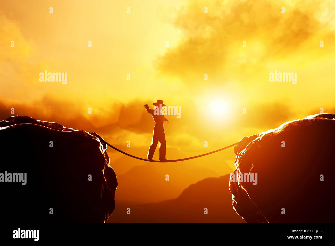 Man in hat walking and balancing on rope over precipice in mountains at sunset. Concept of business Stock Photo