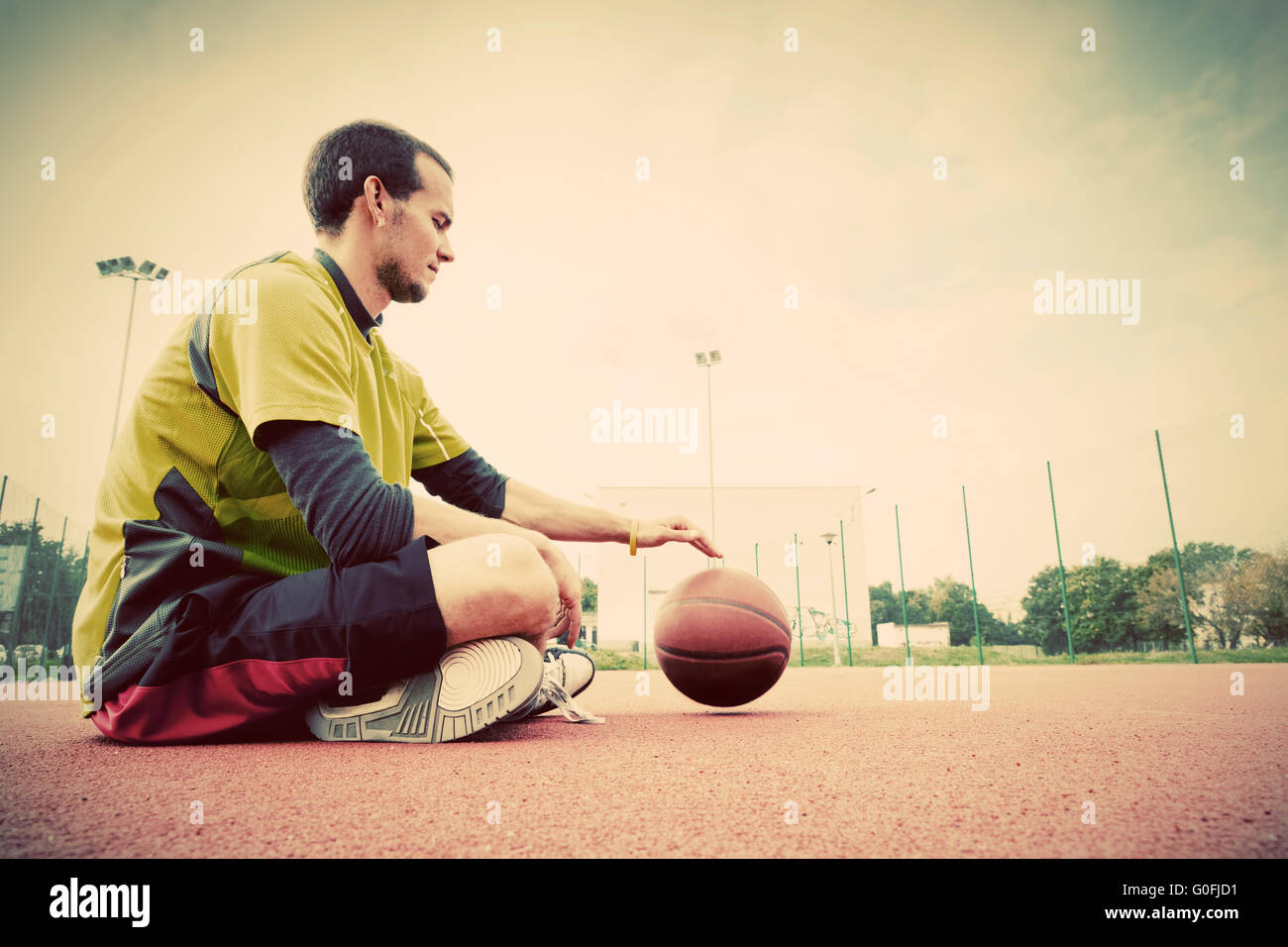 Young man on basketball court. Sitting and dribbling with ball Stock Photo