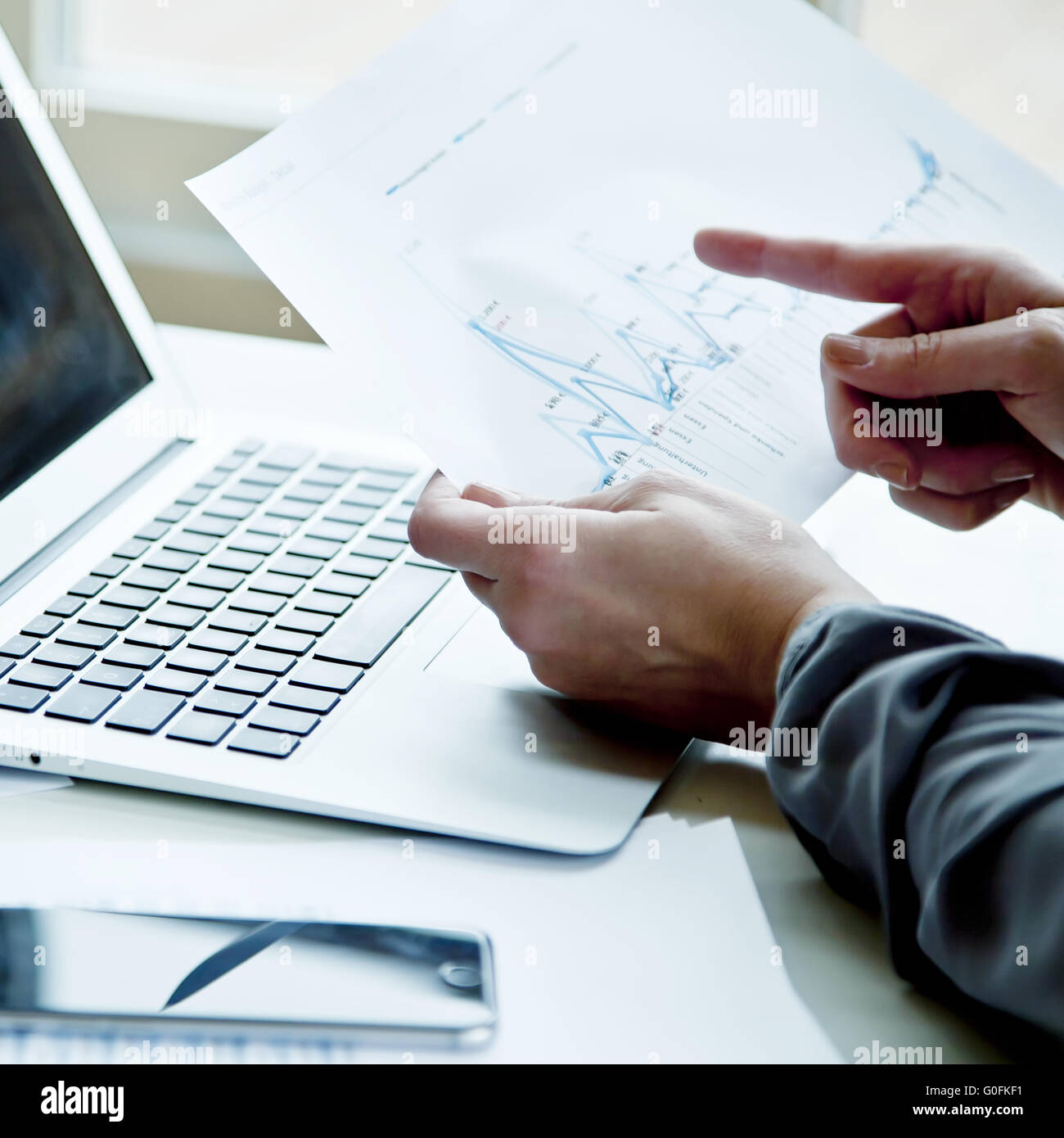 Pessoa usando notebook branco enquanto aponta para gráficos em uma folha