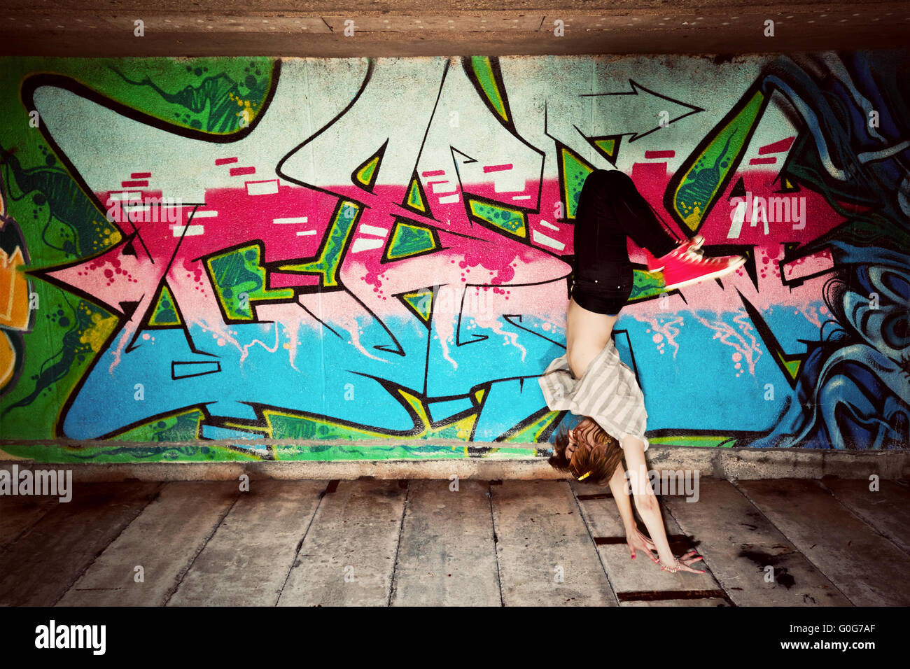 Stylish fashionable girl in a dance pose against colorful graffiti wall. Fashion Stock Photo