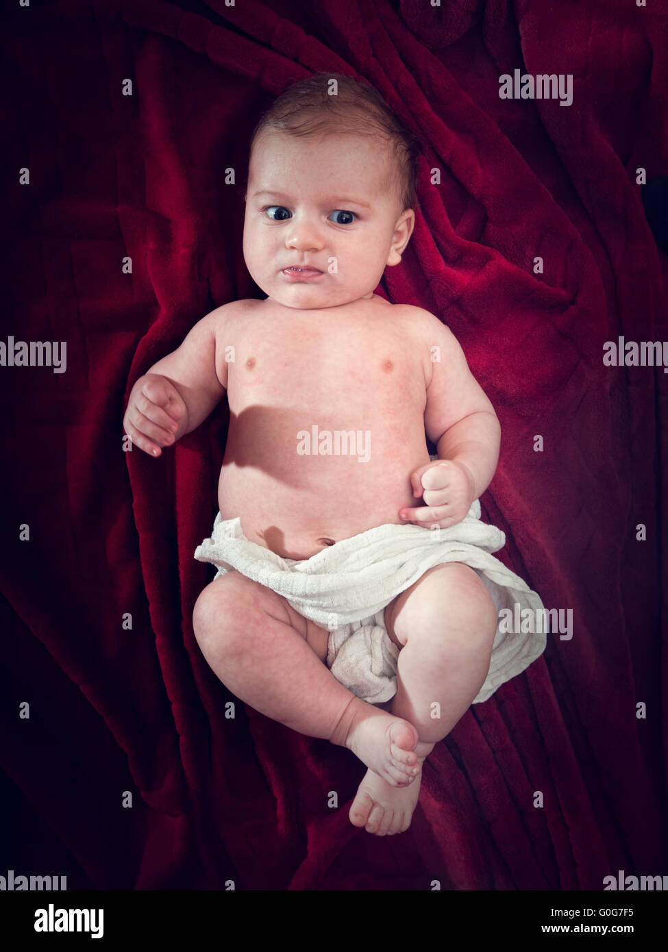 Cute 3 months baby lying on cosy red blanket. Full body view from the top. Stock Photo
