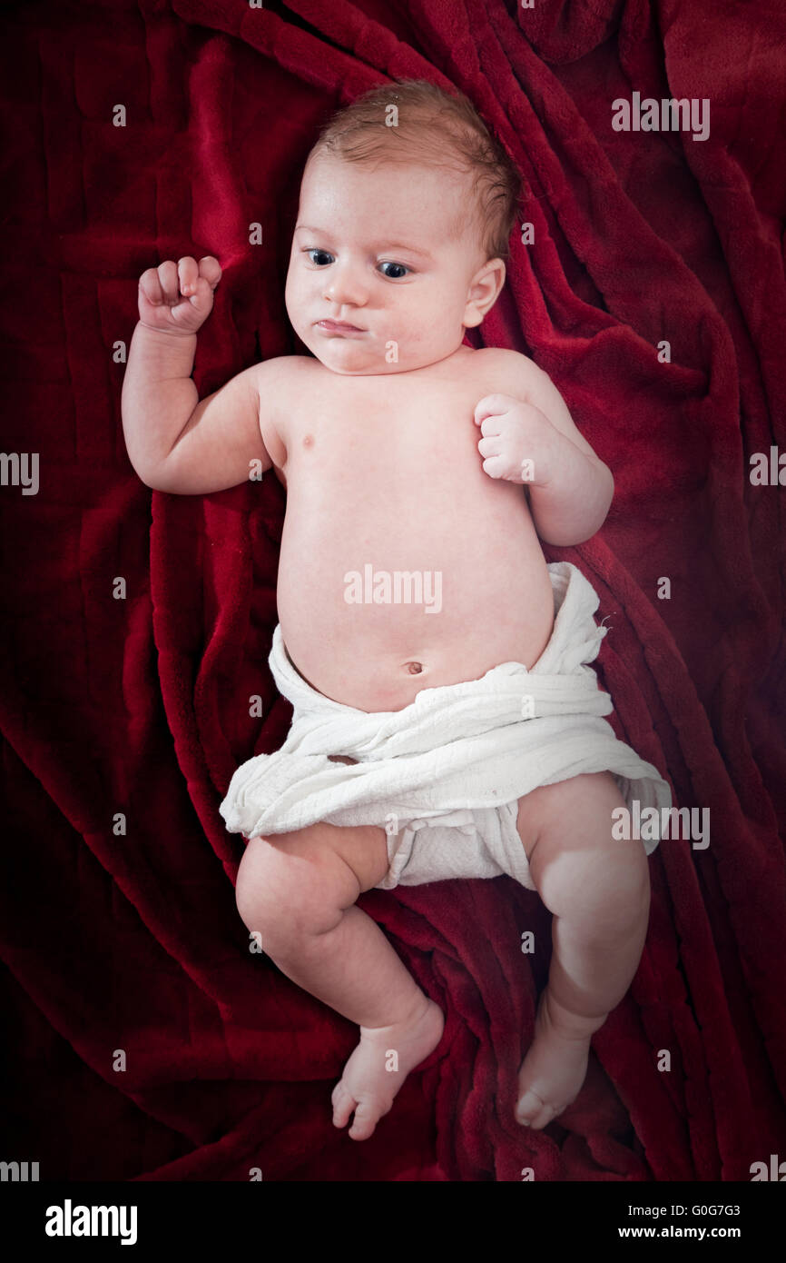 Cute 3 months baby lying on cosy red blanket. Full body view from the top. Stock Photo