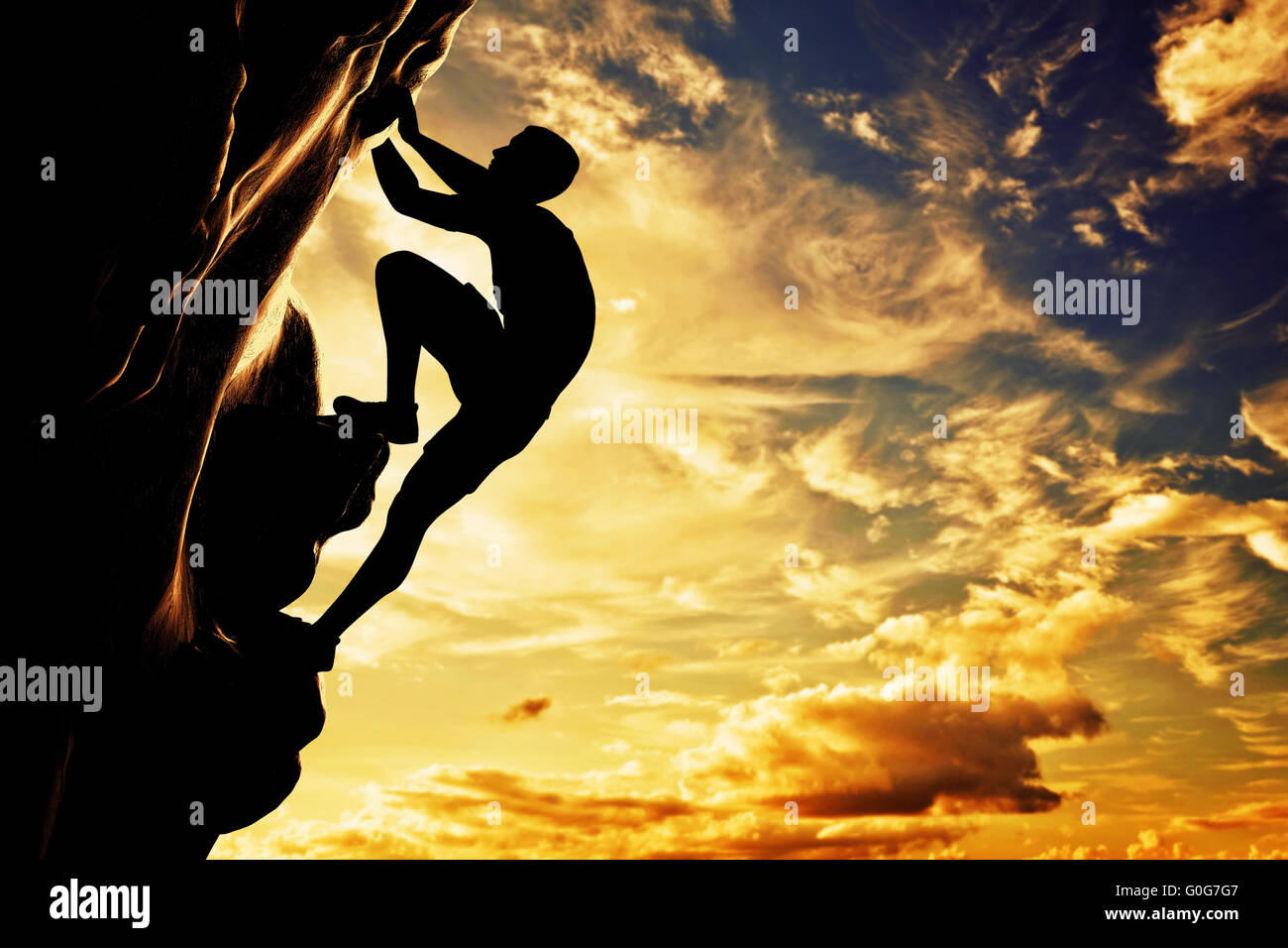 A silhouette of man climbing on rock, mountain at sunset. Adrenaline, strenght, ambition Stock Photo