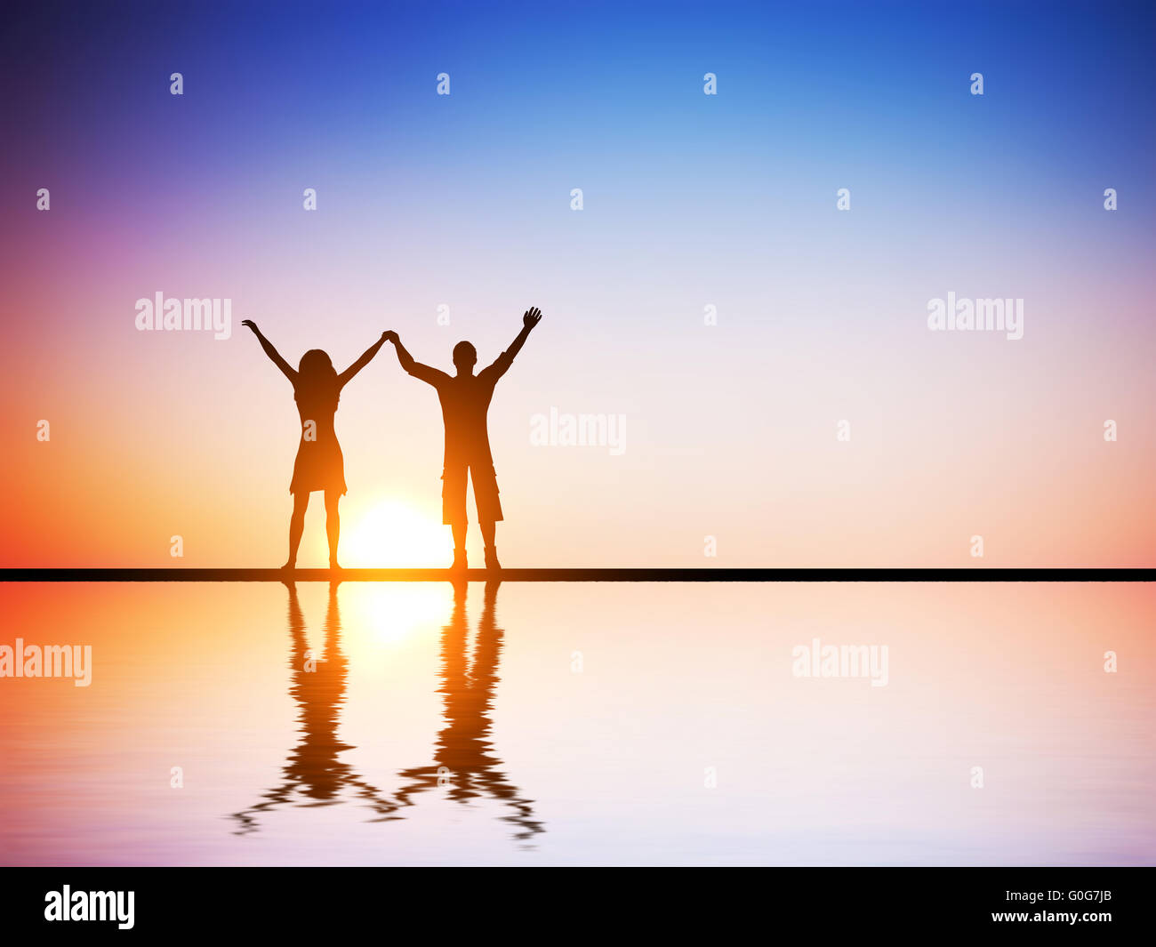 A happy couple in love standing together with hands raised at sunset with water reflection Stock Photo