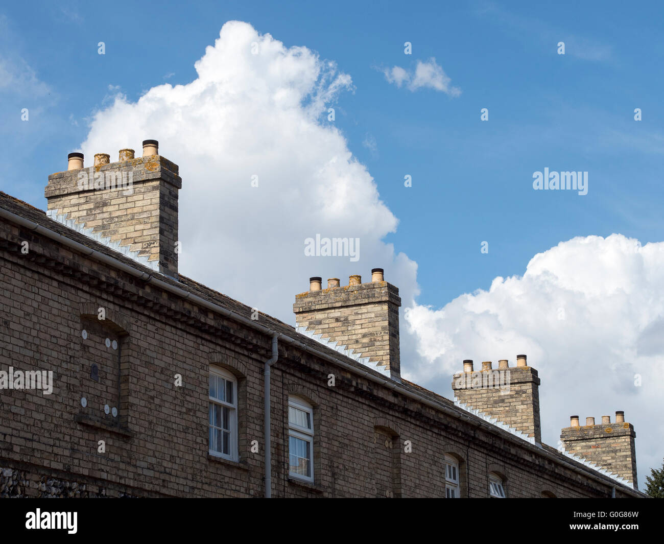 A row of brick chimneys on the roof of a row of terraced houses. Stock Photo