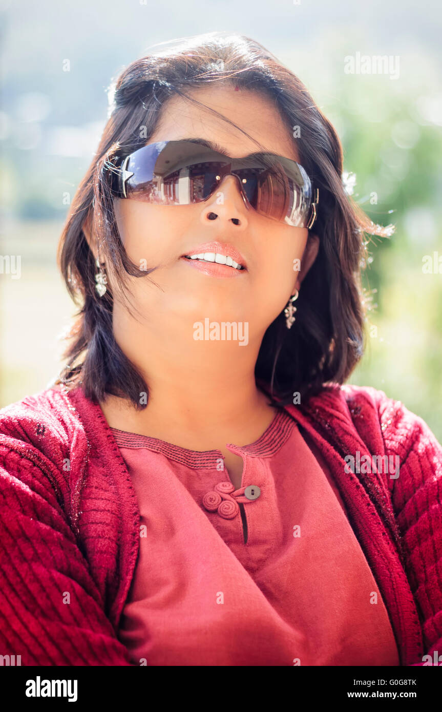 Portrait of a mature, Asian, Non-Caucasian, Bengali beautiful smiling lady with copy space wearing red dress and backlit Stock Photo