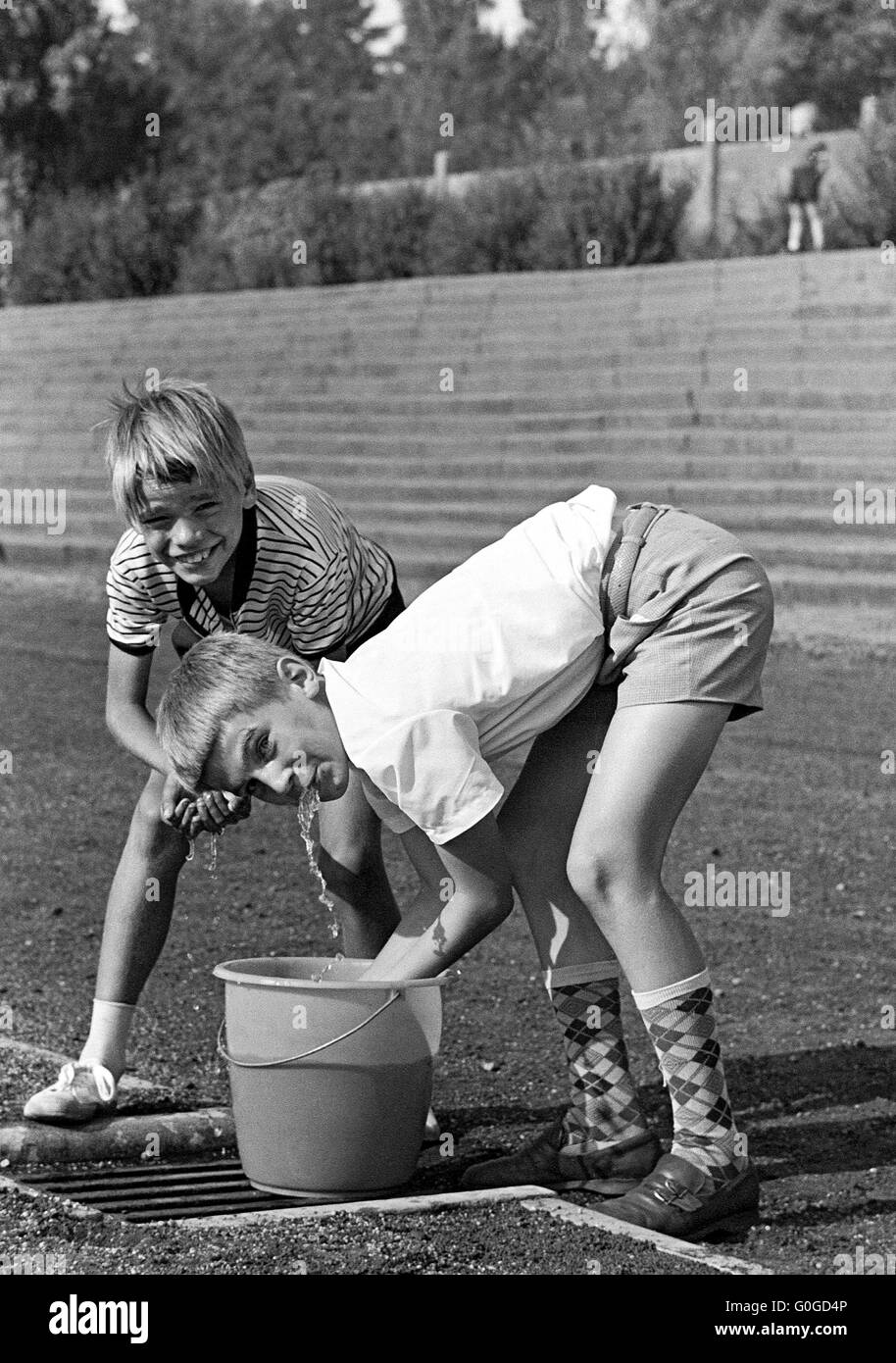 Sixties, black and white photo, people, summer heat, two boys 10 to 13 years refreshing at a water bucket, short trousers, knee-length socks Stock Photo