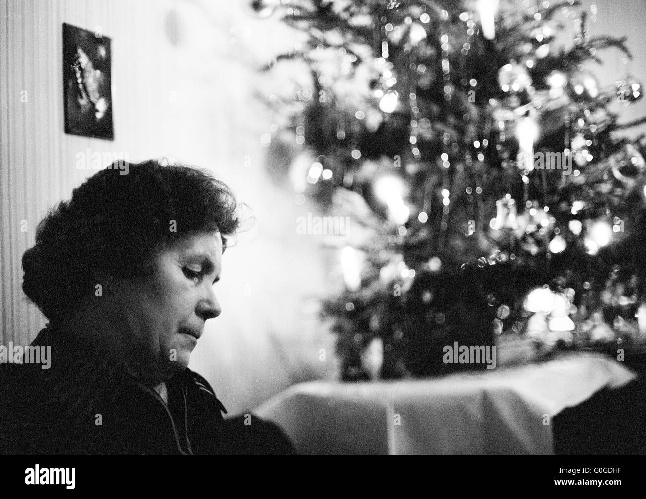Seventies, black and white photo, people, woman 50 to 65 years lonely sitting in the living room, behind the Christmas decoration, loneliness, sadly, depressed, thoughtful Stock Photo