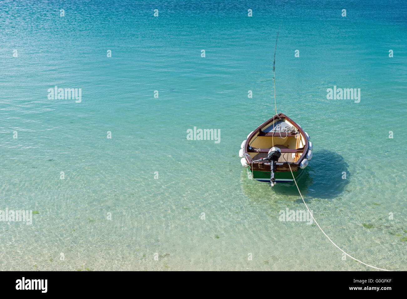 Solitary Dinghy Boat on a clear aquamarine sea with mooring rope Stock Photo