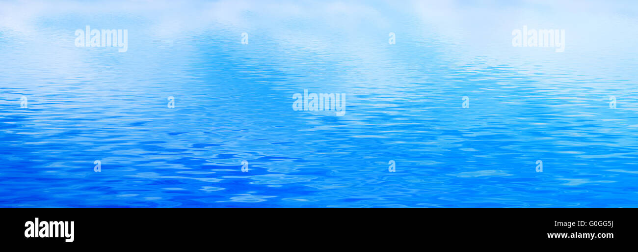 Clean water background with calm waves. Blue sky reflection. Banner Stock Photo
