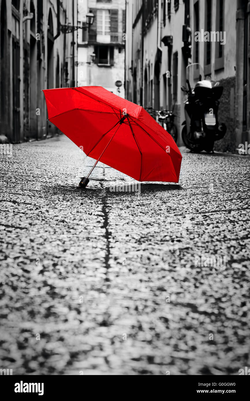 Red umbrella on cobblestone street in the old town. Wind and rain Stock Photo