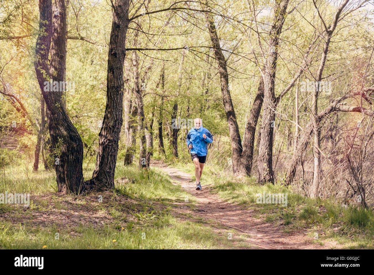 A senior man worn in black and blue is running in the forest, during a warm spring day Stock Photo