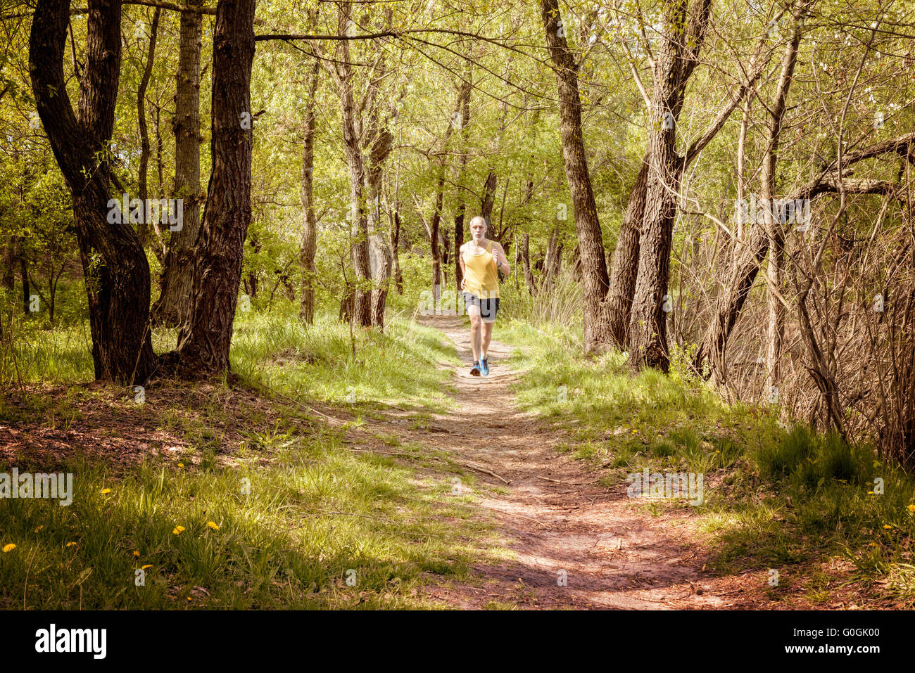 A senior man worn in black and yellow is running in the forest, during a warm spring day evening Stock Photo