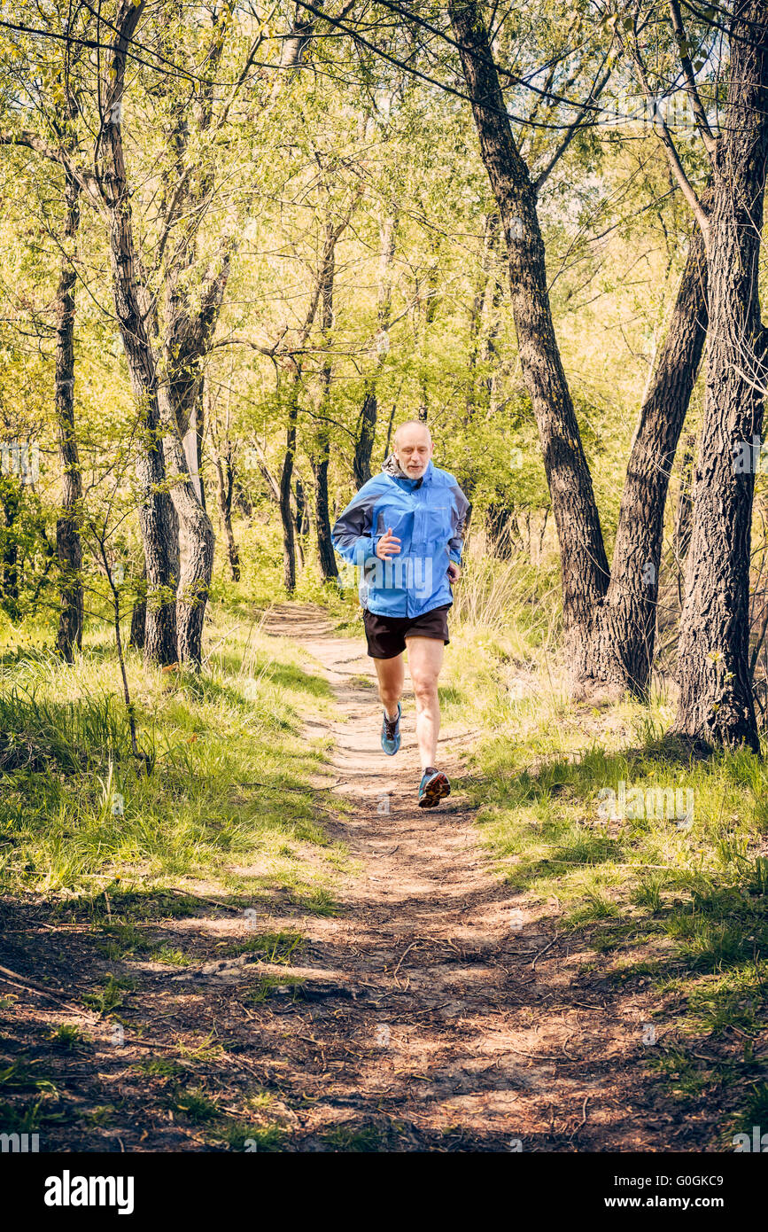 A senior man worn in black and blue is running in the forest, during a warm spring day Stock Photo