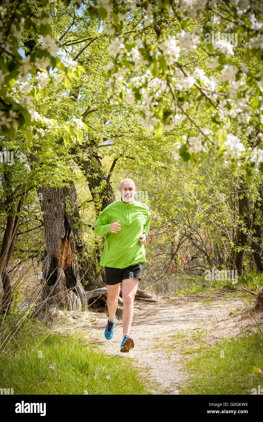 A senior man worn in black and green is running in the forest during a warm spring day Stock Photo
