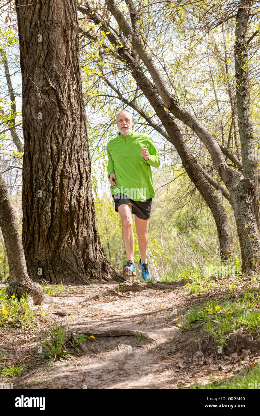 A senior man worn in black and green is running in the forest, during a warm spring day Stock Photo