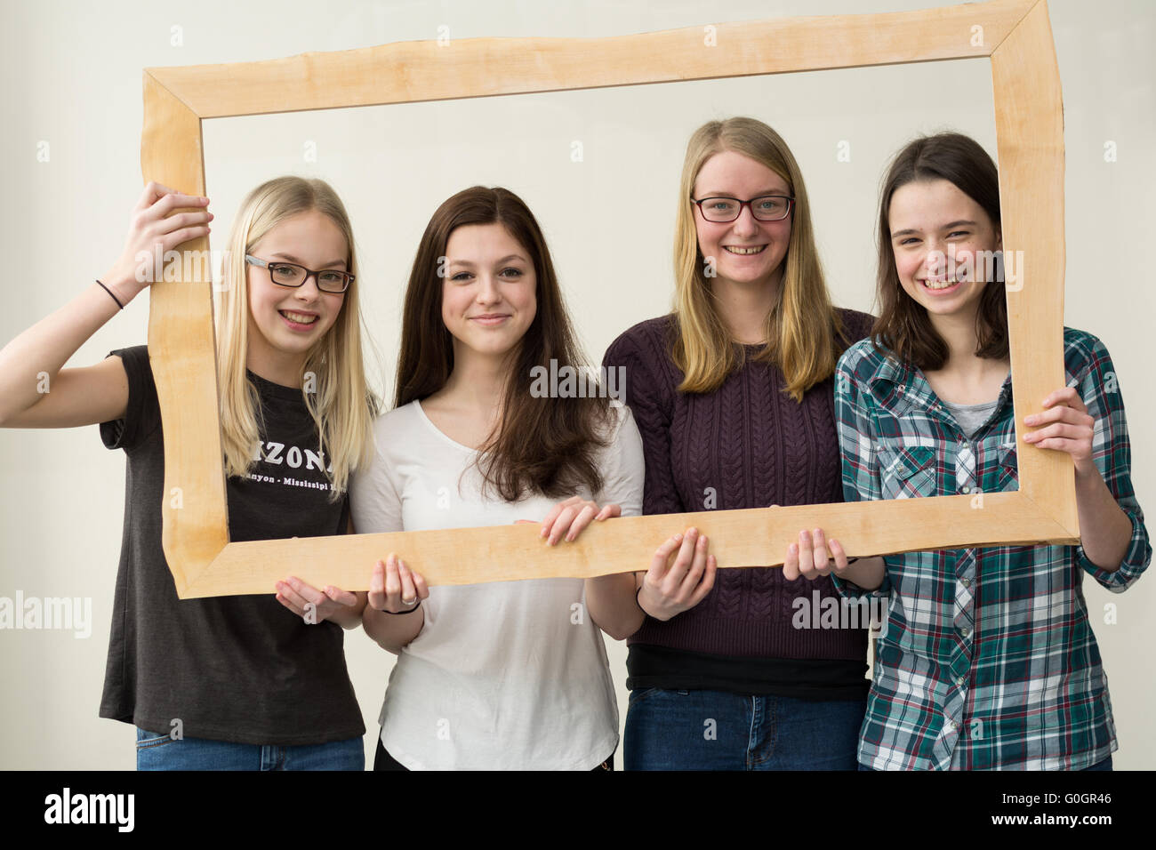 four teenage girls laughing and grinning through a wooden picture frames Stock Photo
