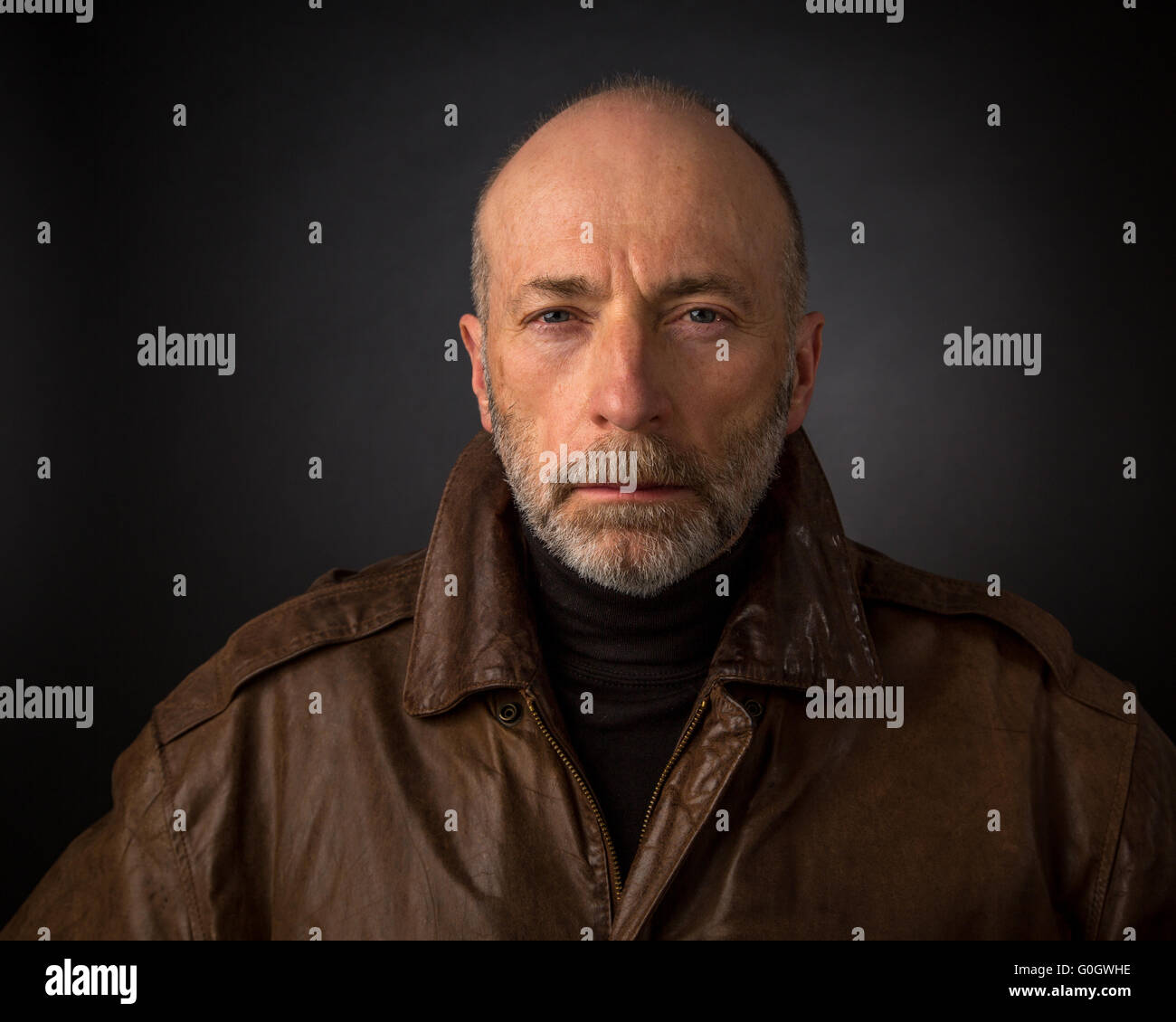 serious and focused senior man in leather jacket - a headshot against a black background Stock Photo