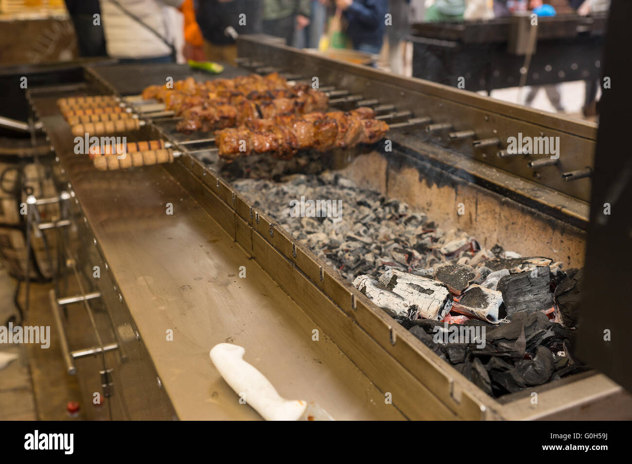 Meat cooking on metal skewers over a lang barbecue fire with hot coals at a catered event or